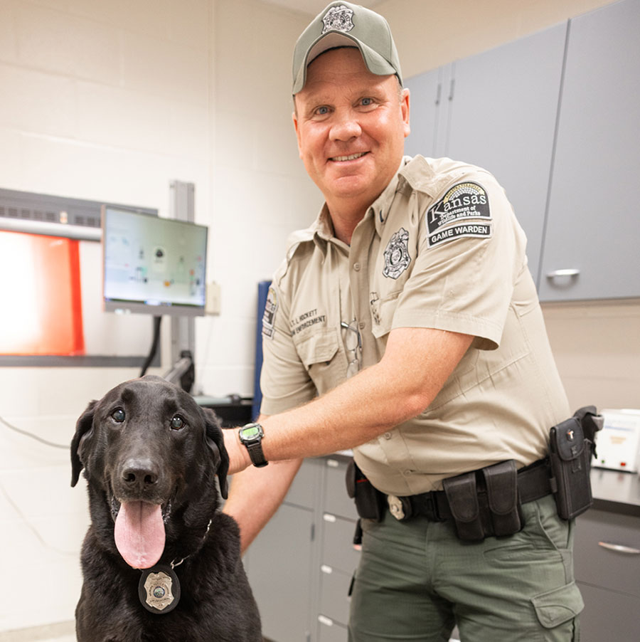 A man in uniform stands proudly, holding a dog on a leash, showcasing a bond between them.